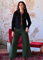 woman wearing long sleeve pink boat neck top and green corduroy pants with black corduroy jacket over the top 