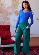 Woman wears electric blue long sleeve top with teal wide leg corduroy pants with a wide waistband, with her hand in pocket