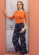 Model wears blue, orange and white floral print on dark blue base cotton corduroy pants with one hand in pocket.