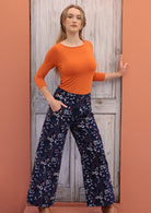 Woman wears wide leg corduroy pants with a wide waistband and pockets, in a floral print on dark blue base.