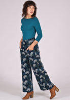 Model poses in blue, green and white floral print on dark blue base cotton corduroy pants, paired with teal stretch top