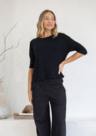 Woman wearing a relaxed fit black top with 3/4 sleeves with hand on hip