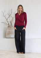 Woman wearing a maroon crossover long sleeve top paired with black pants with hands in pockets