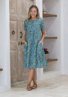 Woman standing with both the hands in pocket wears short sleeved loose fit cotton dress with round neckline.