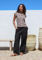 Woman wearing grey floral shirt with high waisted wide leg black cotton pants featuring tapered and pleated ankles  