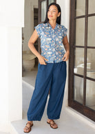 Woman stands wearing a dark blue 100% cotton wide leg pants with pleats at the ankles that slightly taper