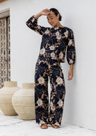 Model wears matching cotton top and pants featuring high waist, side zipper and pockets in black based floral print