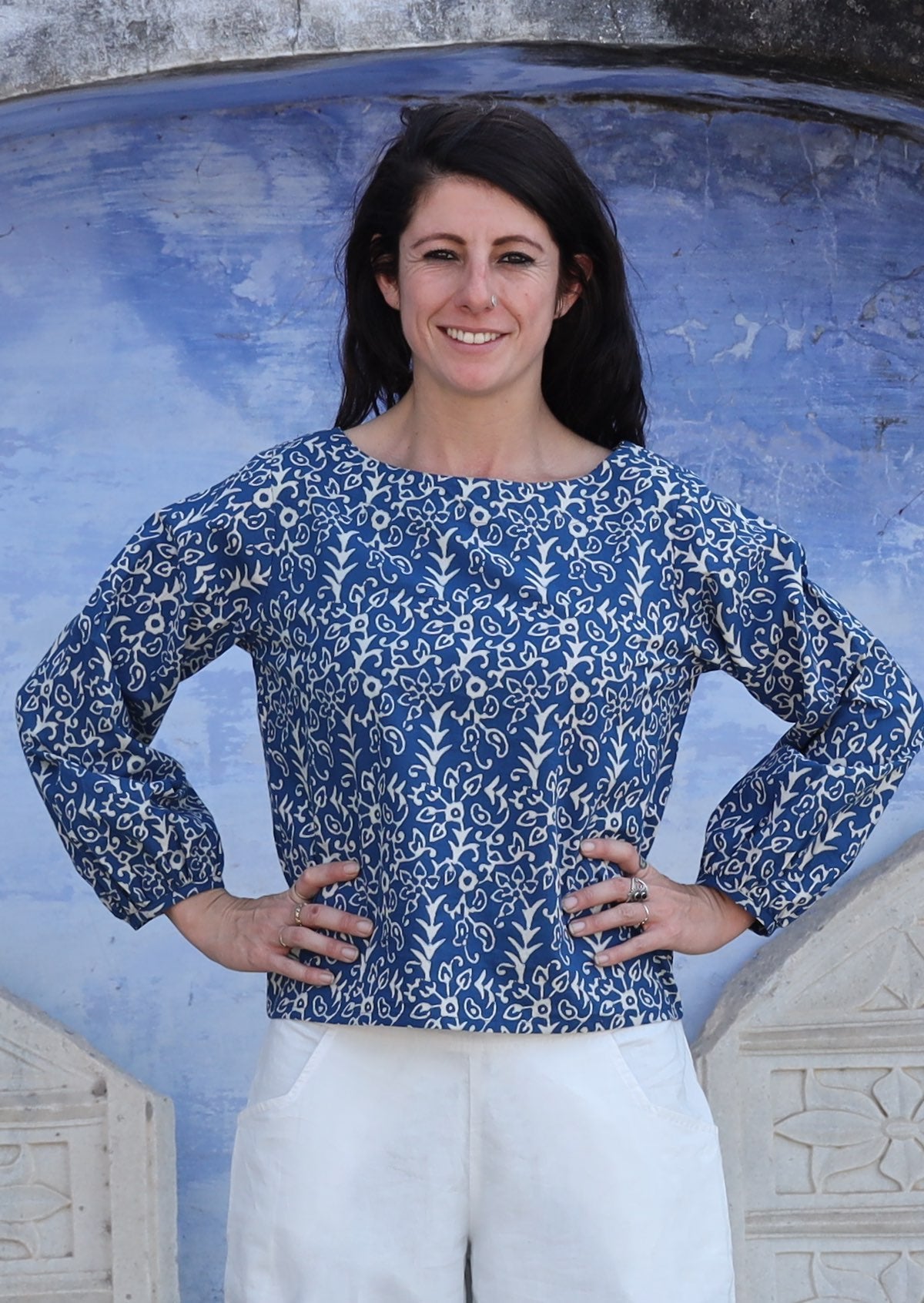 Woman with hands on waist wears top with round boat neckline and Bishop sleeves. 