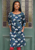 Model poses in front of door in blue, green and white floral on dark blue base cotton corduroy dress