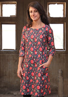 Woman with hand in pocket wearing long sleeve 100 percent cotton dress with deep blue base and raspberry red floral print 