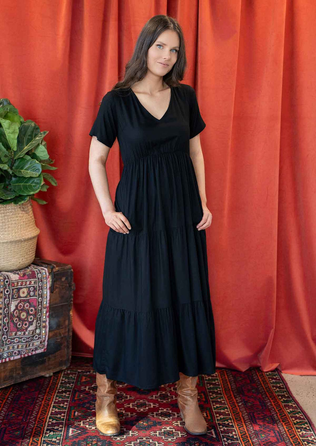 Woman wearing a black rayon dress with short sleeves, a tiered skirt, with her thumbs in side pockets