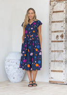 Woman wearing a cotton buttoned bodice with collar, navy dress with multi-coloured spots with hand in pocket