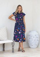 Woman wearing a cotton midi length dress with cap sleeves, a buttoned bodice and waist tie