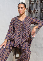 Model sitting on a wooden stool wears lightweight 100% cotton long sleeve, button through top in dark purple based floral print.