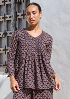 Woman in cotton long sleeve button through top with small pleats across chest in dark purple based floral motif print.