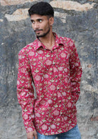 Man wears long sleeve cotton button through shirt, in cranberry based Indian floral print