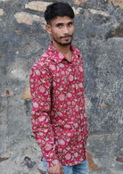 Man wears long sleeve cotton button through shirt with collar and coconut buttons, in cranberry based floral print