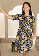 Woman wearing a relaxed fit, above knee length retro floral cotton dress with yellow and grey floral print on a black base