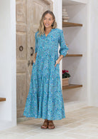 Woman with both the hands in pocket wears 3 tiered maxi dress with mandarin collar and V neckline.