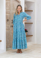 Model with her hand on hip wears 100% cotton white and blue floral print maxi dress with buttoned bodice.