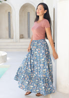 Woman wearing a pink top and a floaty blue cotton floral maxi skirt standing in a bright, architectural space