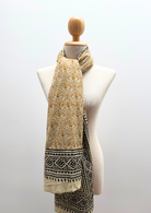 A lightweight scarf with a mustard yellow floral pattern and a black geometric border, draped on a cream-colored fabric mannequin torso against a light gray background.