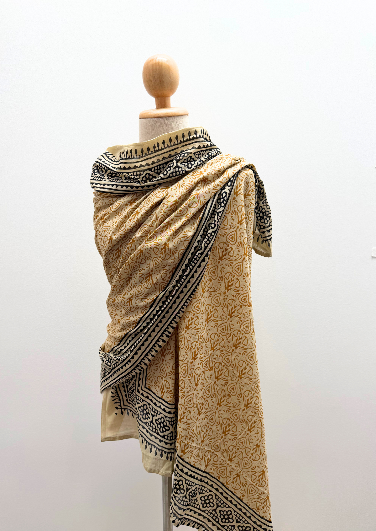 A beige and black patterned shawl draped on a wooden dress form mannequin against a plain white wall.