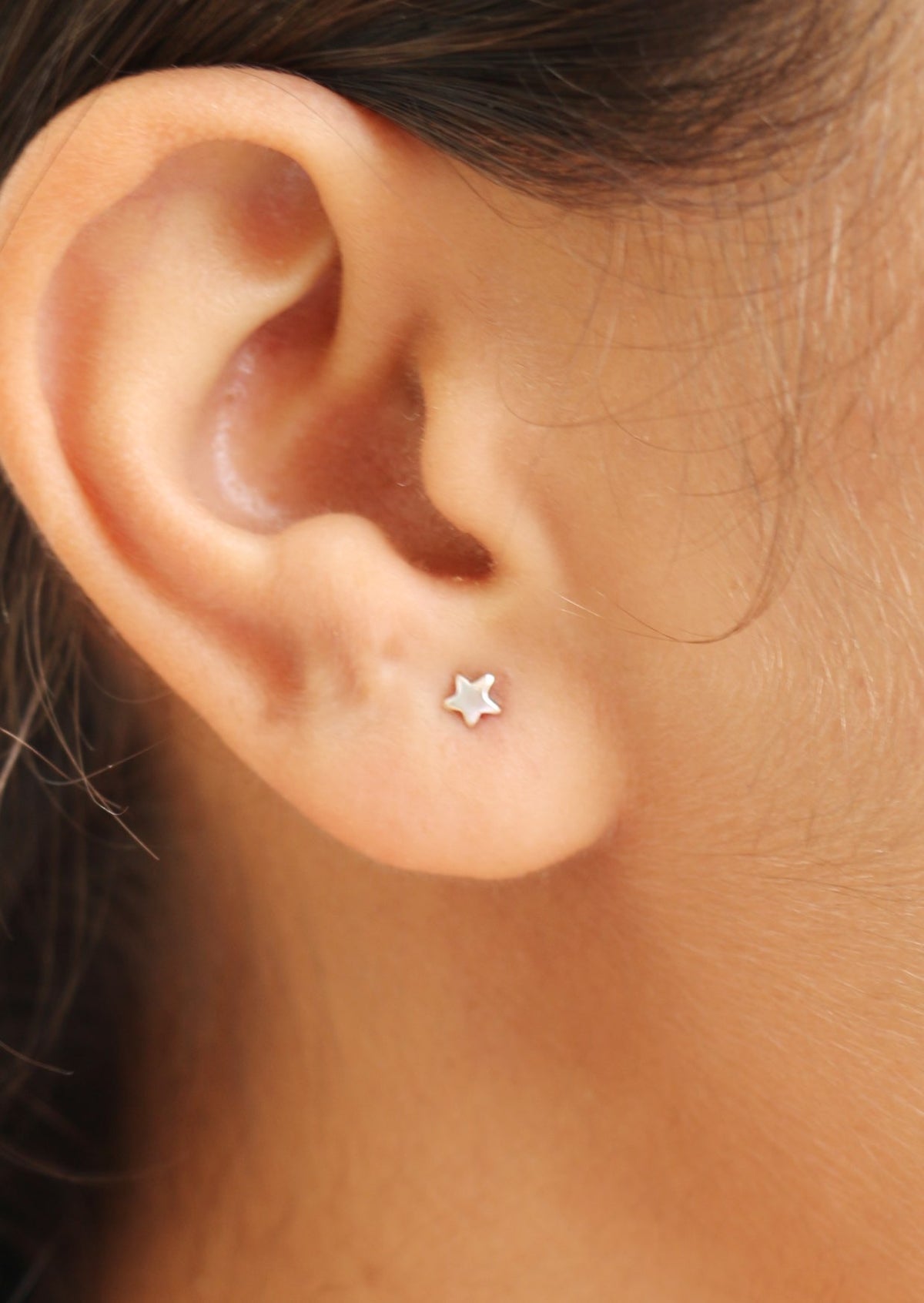 Close-up of an ear wearing a minimalist star shaped silver studs with butterfly backs