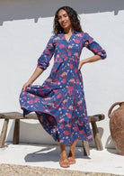 Woman poses in blue floral cotton maxi dress with buttoned bodice, 3/4 sleeves and flowy three tiered maxi skirt