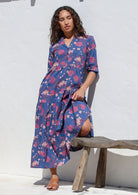 Woman standing in navy blue cotton flowy tiered maxi dress with 3/4 sleeves, buttoned bodice and pockets 