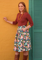Woman wearing a pastel print cotton knee length skirt and rust top against a yellow wall.