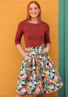Woman wearing Ruby knee length skirt with belt loops, button down front, box pleats and pockets in pastel spotted print