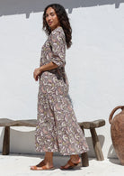 Woman standing in front of wooden bench wears three tiered cotton maxi dress with 3/4 sleeves, pockets and mandarin collar