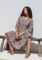Woman sits on a wooden bench posing in lightweight cotton floral printed maxi dress with 3/4 sleeves, mandarin collar and buttoned bodice