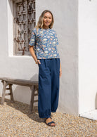 Woman wearing a blue floral cotton boxy top with short sleeves and a high round neckline, paired with dark blue cotton pants.