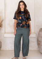 Woman standing in a black based botanical print top featuring grey, green and blues with orange and pink florals.