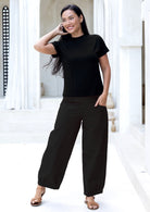 Woman wearing a black wide legged cotton pants standing in a bright, minimalistic room.