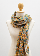 A patterned scarf draped on a cream-colored fabric mannequin torso with a wooden neck cap, set against a plain white background.