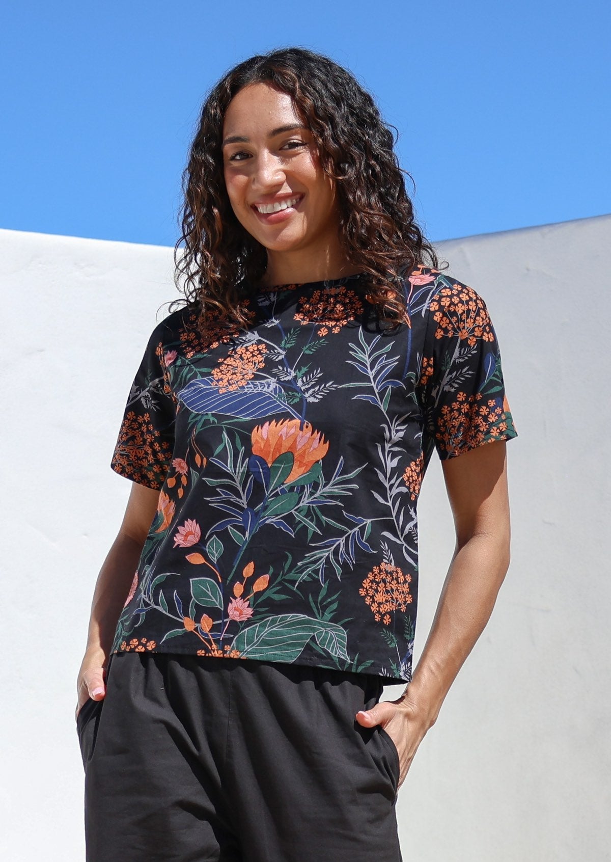 Woman wearing a loose fitting black floral cotton top with short sleeves and high round neckline