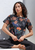 Woman wearing a 100% cotton loose fitting black top with short sleeves, round neckline and button back closure