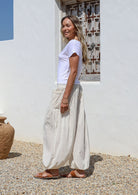 Woman wearing a white t-shirt and white wide-leg cotton pants standing in front of a white wall 