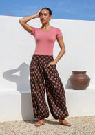 Woman posing in earthy brown floral printed cotton harem pants with wide flat front waistband  and elasticated ankles.