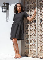 Woman posing in a loose fitting black cotton dress with short sleeves, gathers at the waist and round neckline