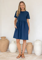 Model wears sea blue cotton dress with length above the knee, pockets and small gathers at the loose waist