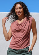 Woman wearing a pink sleeveless cowl neck top with a blue sky background