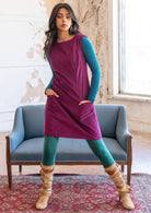 Woman wears bright plum purple corduroy sleeveless tunic with high round neckline and deep pockets