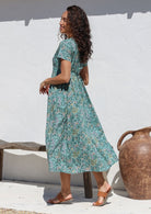 Model poses in 100% cotton sage green floral midlength dress with shoestring tie, side pockets, short sleeves and V neckline