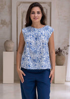 Woman wearing a white based blue floral cotton top with dark pants in an indoor setting.