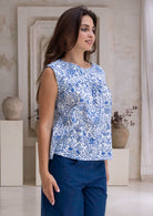 Woman wearing a white based blue floral, 100% cotton top in an indoor setting.