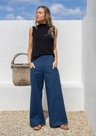 Woman wearing blue cotton wide leg pants with a wide waistband, side zipper, and pockets, standing against a white wall
